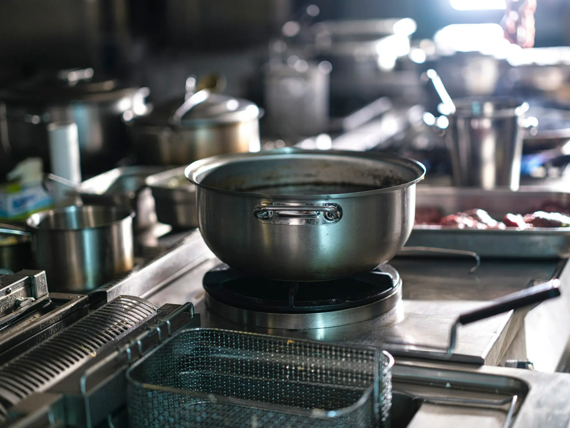 Stainless steel pots and a deep fryer basket on a busy commercial kitchen stove, the kind of equipment that drives a café's power and gas bill