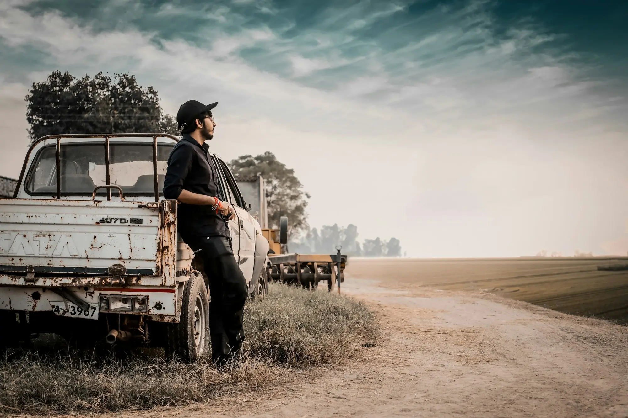 A farmer standing beside his ute on a dirt farm track in the open countryside.