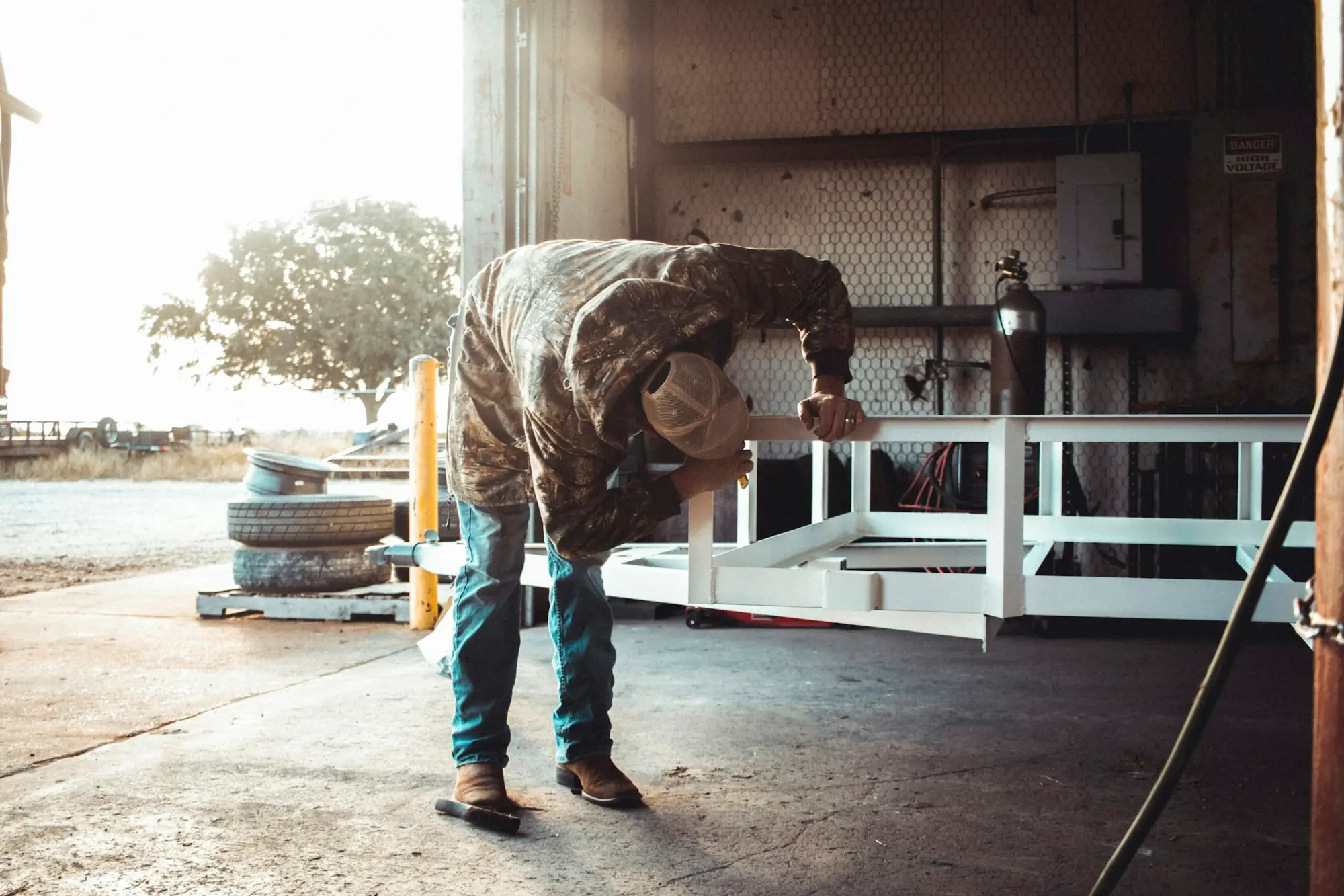 A truck driver bending down at the back of a freight truck to check the load.